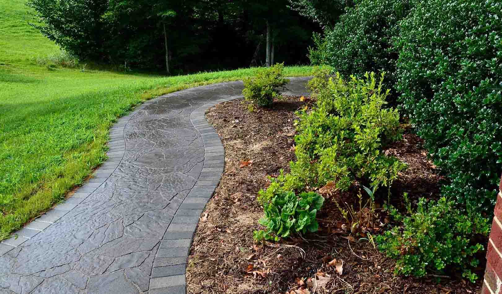 Stamped concrete walkway with a natural stone pattern and contrasting border, curving through landscaped garden beds.