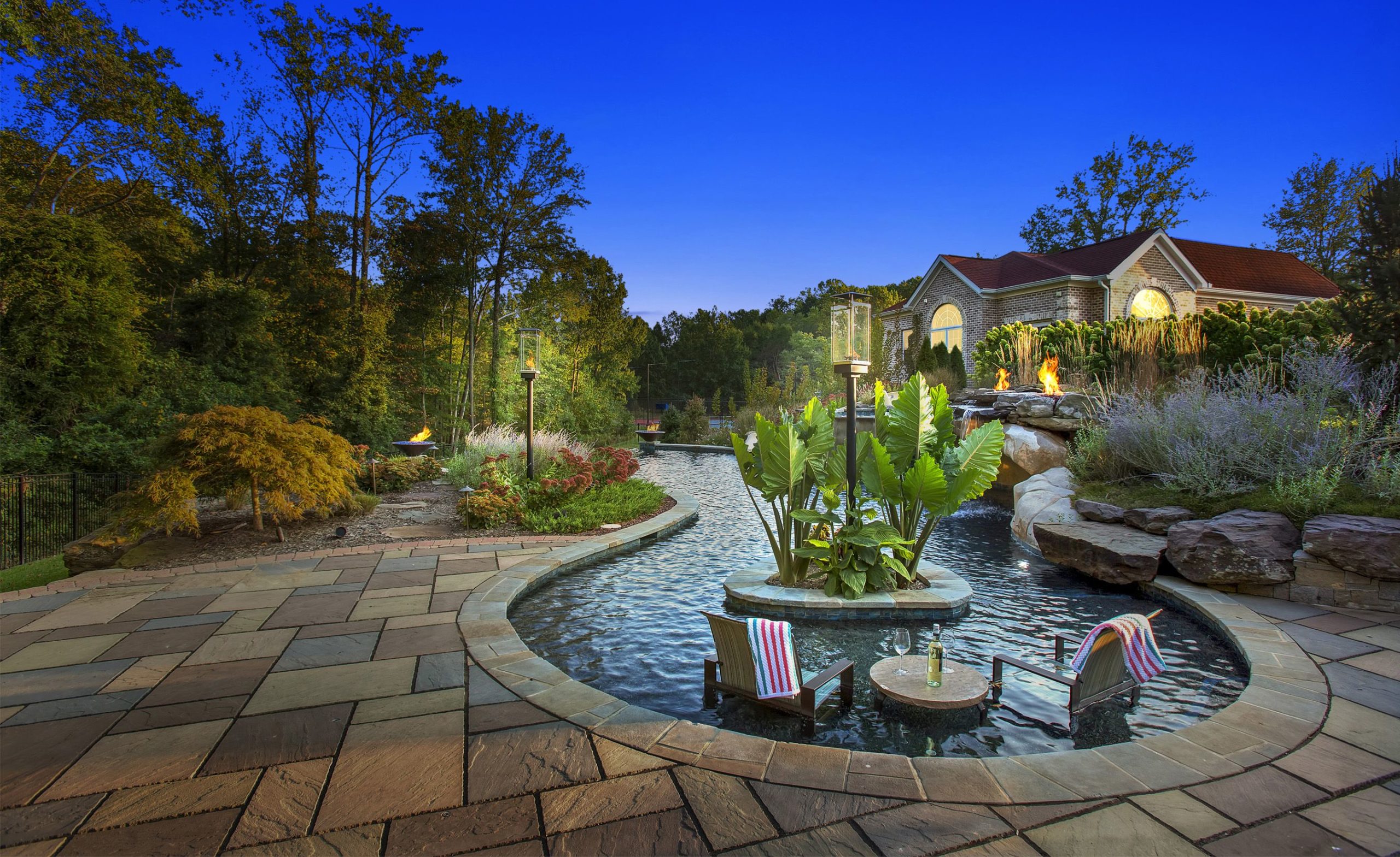 Luxury backyard with custom stone patio, pool, and integrated landscape lighting at dusk