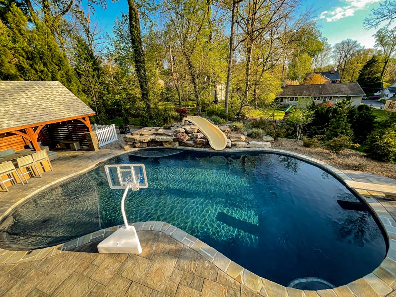 Kidney shaped pool with small waterslide and basketball hoop