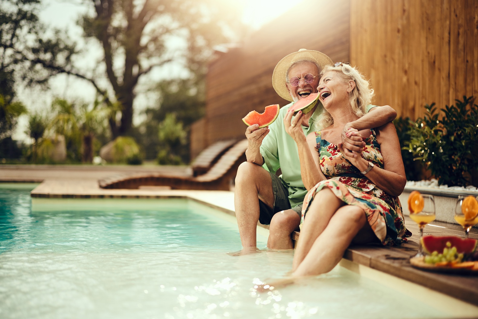 Cheerful senior couple eating watermelon by the pool.